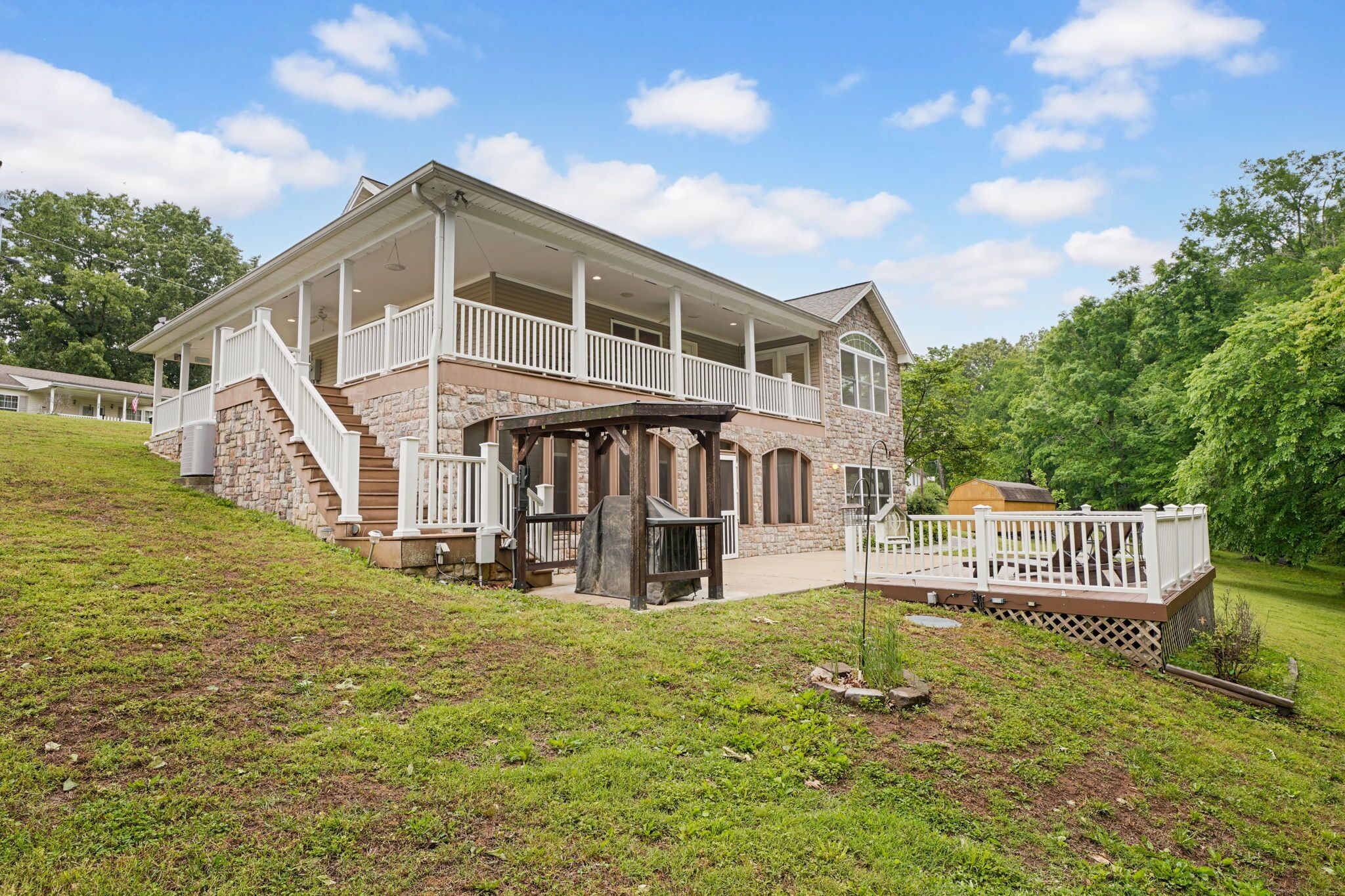 A two-story house with a covered porch, stone exterior, and a small deck.