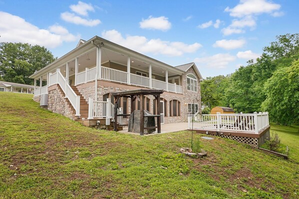 A two-story house with a covered porch, stone exterior, and a small deck.