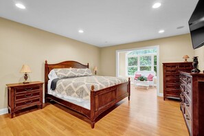 A bedroom with a wooden bed, a dresser, a nightstand, and a television.