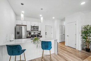 Una cocina moderna con armarios blancos, electrodomésticos de acero inoxidable y dos taburetes azules.