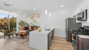 A modern kitchen with a central island, stainless steel appliances, and a large window overlooking a tree. - Bright 1BD Sleeps 2 Near Liberty Bell Center City (Philadelphia)