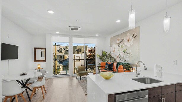 A modern kitchen with a central island, a dining area with a white table and chairs, and a living area with a sofa and a painting. - Bright 1BD Sleeps 2 Near Liberty Bell Center City (Philadelphia)