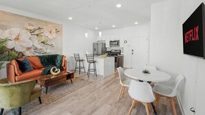 A modern living room with a sofa, coffee table, and chairs, a kitchen with a microwave and refrigerator, a dining area with a table and chairs, and a wall-mounted TV. - Bright 1BD Sleeps 2 Near Liberty Bell Center City (Philadelphia)