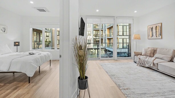 A modern hotel room with a bed, a sofa, a TV, a plant, and a balcony with a view of the city. - Chic 1BD Sleeps 2 Near Independence Hall Philly (Philadelphia)