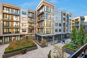 En modern flervåningsbyggnad med bostäder, balkonger, stora fönster och en vackert anlagd innergård.