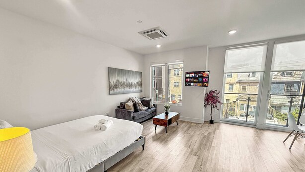 Un dormitorio moderno con cama, sofá, televisor y un ventanal grande.