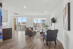 A modern living room with a sofa, armchair, and coffee table, large windows with a city view, and a flat-screen TV mounted on the wall. - Stylish Studio Sleeps 2 Near Reading Terminal PA (Philadelphia)