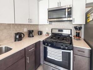 A modern kitchen with stainless steel appliances, including a microwave, stove, and coffee maker. - Charming Studio Sleeps 2 | Walk to Liberty Bell (Philadelphia)