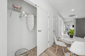A modern interior with a white wall, a white door, a white table with chairs, a plant, and a shelf with items. - Stylish Studio Sleeps 2 Near Reading Terminal PA (Philadelphia)