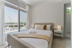 A hotel room with a large bed, two bedside tables, a view of a pool and buildings, and a sliding glass door.