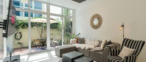 A modern living room with a sofa, a striped armchair, a marble coffee table, a large window, and a ceiling light fixture.