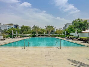 A swimming pool with lounge chairs and umbrellas, surrounded by greenery and modern buildings.