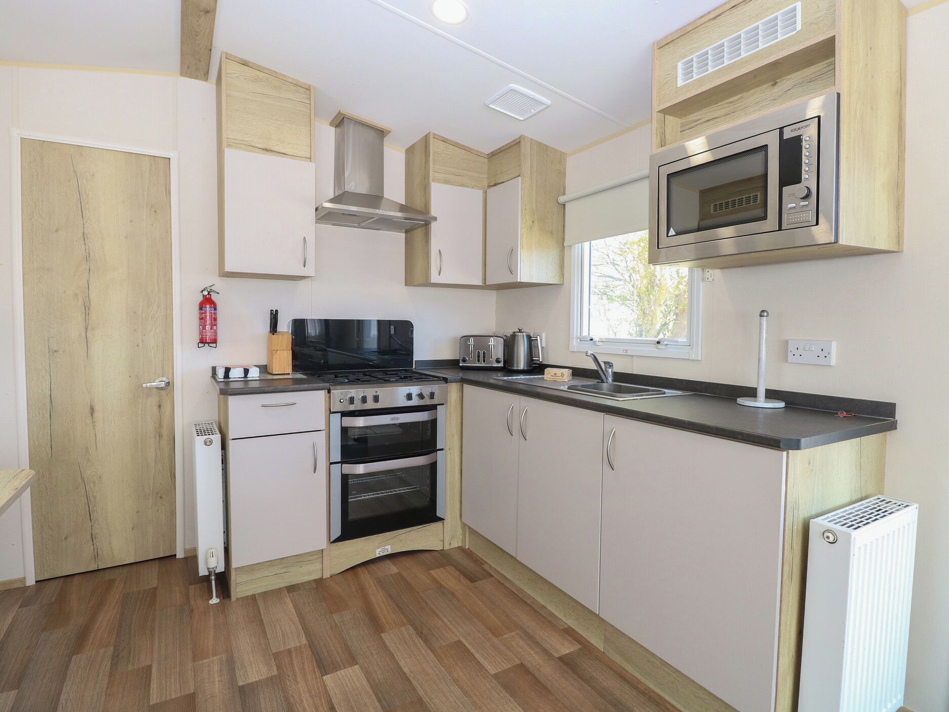 A compact kitchen with a stove, oven, microwave, and a window.