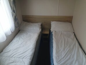 Quarto pequeno e individual com duas camas de solteiro, cabeceira de madeira e janela com cortinas leves.