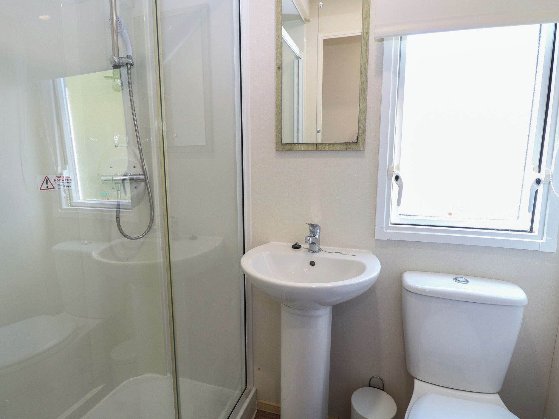 Ein Badezimmer mit Duschkabine aus Glas, einem Standwaschbecken, einer Toilette und einem Fenster für natürliches Licht.