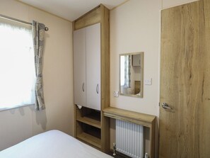 A bedroom with a bed, wardrobe, mirror, radiator, and wooden door. - Caravan 325 (Lowestoft)