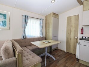 A compact kitchenette with a wooden table, a bench, and a window with curtains. - Caravan 325 (Lowestoft)