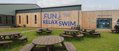 An outdoor pool area with picnic tables and a wooden building with signage for a fun, relaxing swim zone.