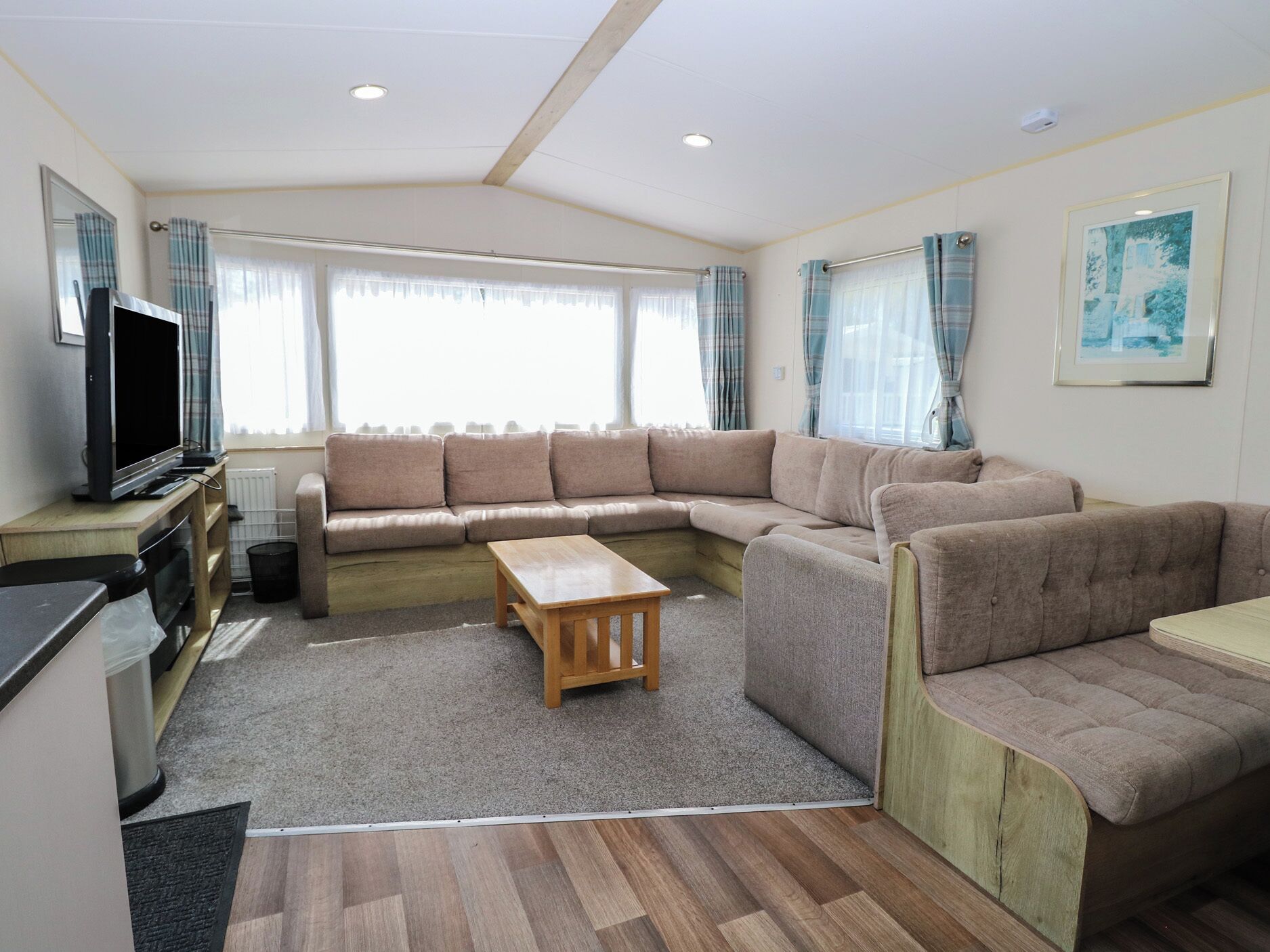 Uma sala de estar com sofá seccional, televisão e mesa de centro de madeira.