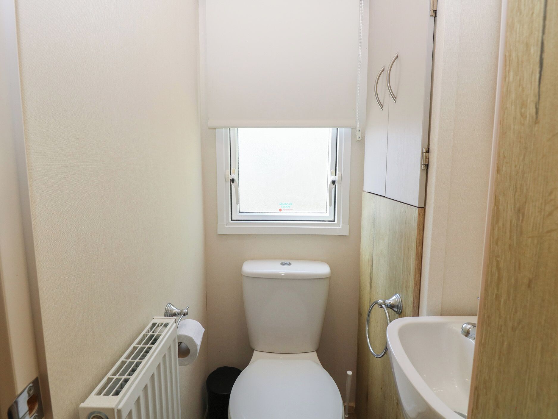 A small bathroom with a toilet, a window, a radiator, and a sink.