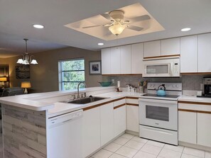 Une cuisine moderne avec des armoires blanches, un lave-vaisselle encastré, une cuisinière et un ventilateur de plafond.