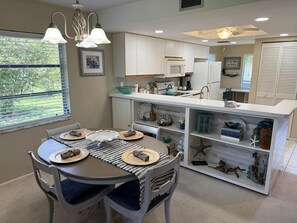 A modern kitchen with white cabinets, a central island, and a dining area with two chairs and a table set for two. - Fiddler’s Green 2BR Getaway (Englewood)