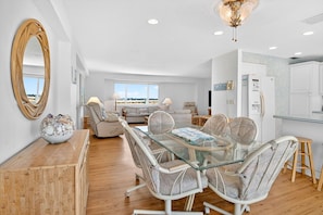 A modern living room with a glass dining table, wicker chairs, a sofa, and a large mirror.