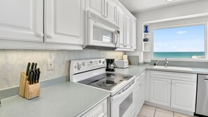 A kitchen with white cabinets, a stove, a microwave, and a view of the ocean.