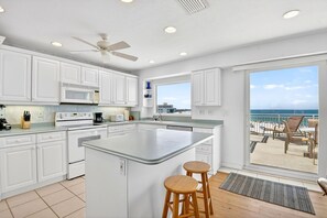 A kitchen with a large island, white cabinets, and a view of the beach.