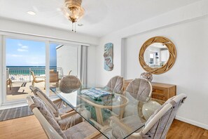 A dining area with a glass table, wicker chairs, a wooden cabinet, and a large mirror on the wall.