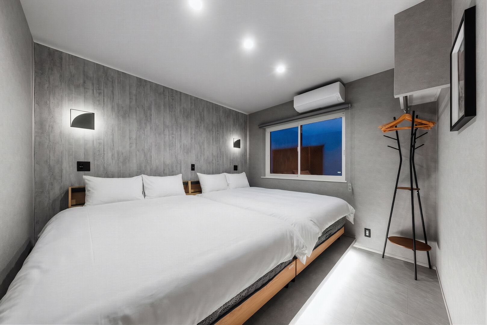 A modern bedroom with a large bed, a window with a view, an air conditioning unit, and a wooden floor.
