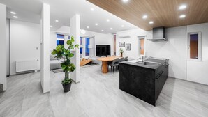 A modern kitchen with a central island, a dining area with a round table, and a living space with a sofa and a TV. - THE POLARIS (Sapporo)