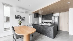 A modern kitchen with a central island, built-in appliances, and a dining area with a wooden table and chairs. - THE POLARIS (Sapporo)