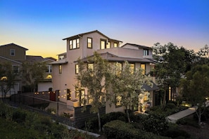 A multi-story residential building with a balcony, a garden area, and a well-lit entrance. - RMV Gem - FamilyFriendly, Amenities, Rooftop Views (Ladera Ranch)