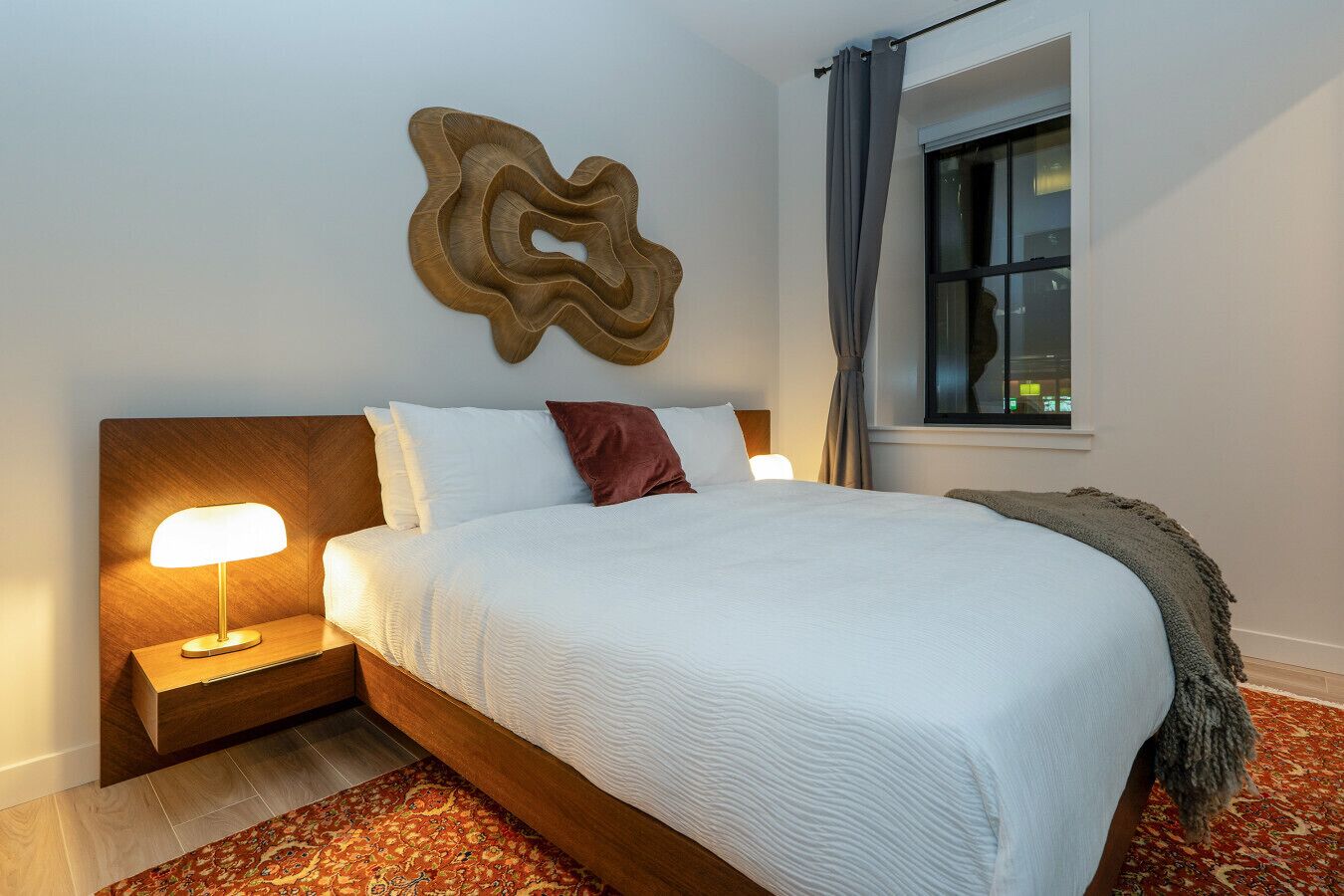 A neatly made bed with white bedding, a wooden headboard, and a decorative wall piece.
