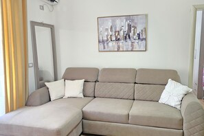 Ein beiges Ecksofa mit zwei Kissen, ein Stadtbild an der Wand und eine Tür links.
