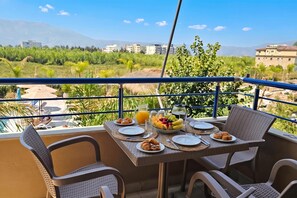 A balcony with a table set for breakfast, overlooking a lush landscape with buildings in the distance.