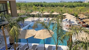 Un espace piscine doté de chaises longues et de parasols, entouré de verdure et avec des montagnes en toile de fond.