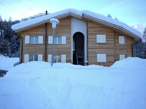 A wooden chalet with a snow-covered roof, a central entrance, and a small porch area. - Bevernage, (Splügen), by Interhome (Splügen)