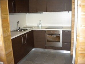A compact kitchen with dark cabinets, a stainless steel sink, a built-in oven, and a countertop. - Bevernage, (Splügen), by Interhome (Splügen)