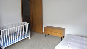 Een slaapkamer met een ledikantje, een houten dressoir en een kledingkast.