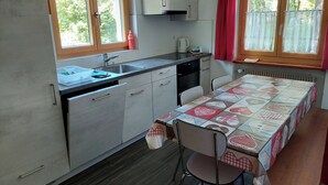 Een kleine keuken met een spoelbak, fornuis en een eettafel.