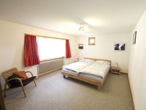 Ein Schlafzimmer mit einem Bett, einem Sessel, einem kleinen Tisch, einem Fenster mit Vorhängen und einer Heizung.