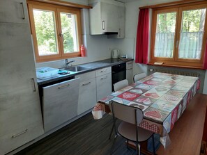 A compact kitchen with a sink, stove, and cabinets. There is a table with a quilted tablecloth and a chair. - Haus Wanner, (Splügen), by Interhome (Splügen)