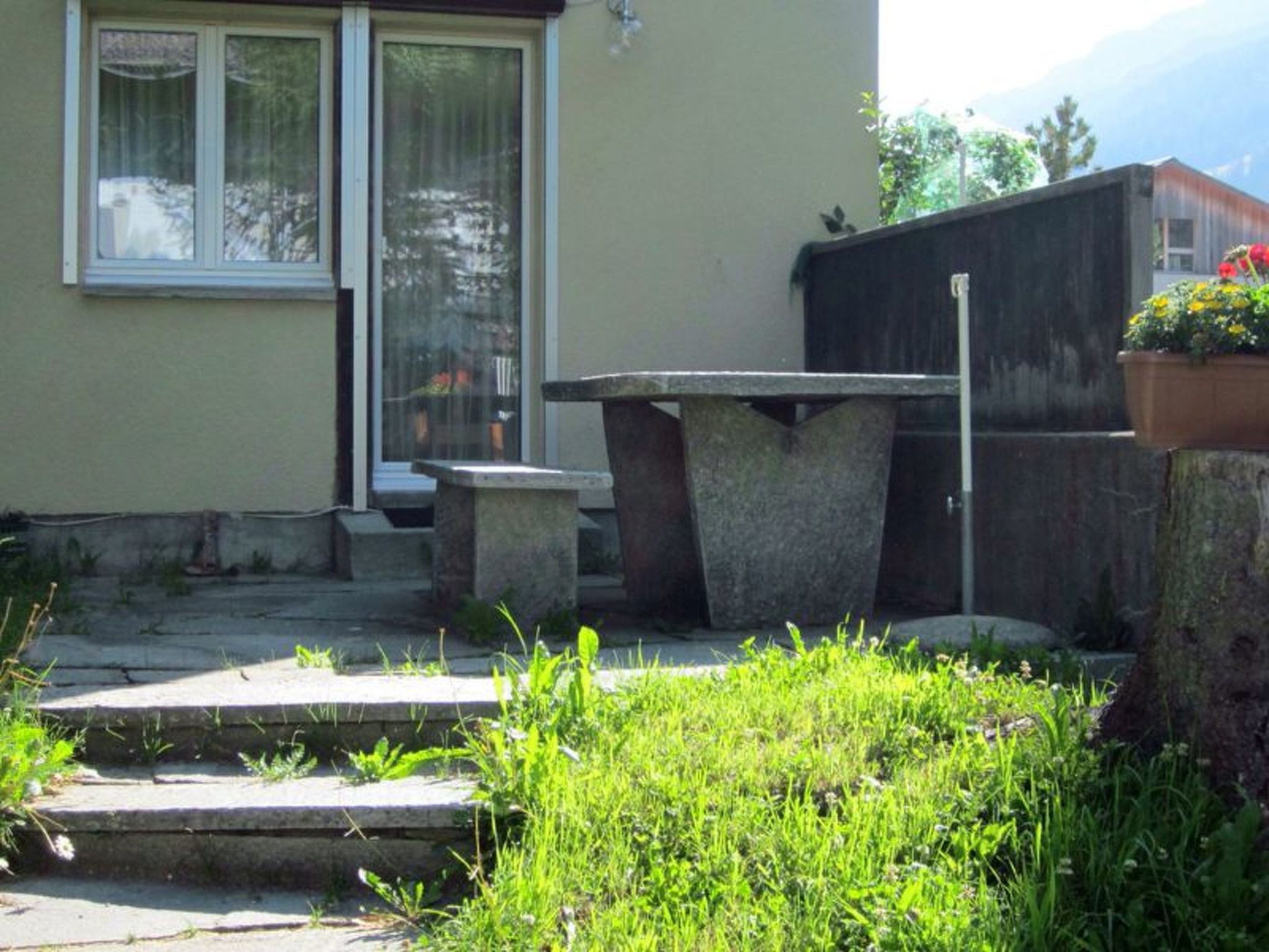 A concrete bench and table in a garden area with steps leading up to a door.