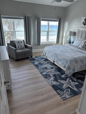 Ein Schlafzimmer mit Bett, Sessel, Nachttisch und Blick auf den Ozean.