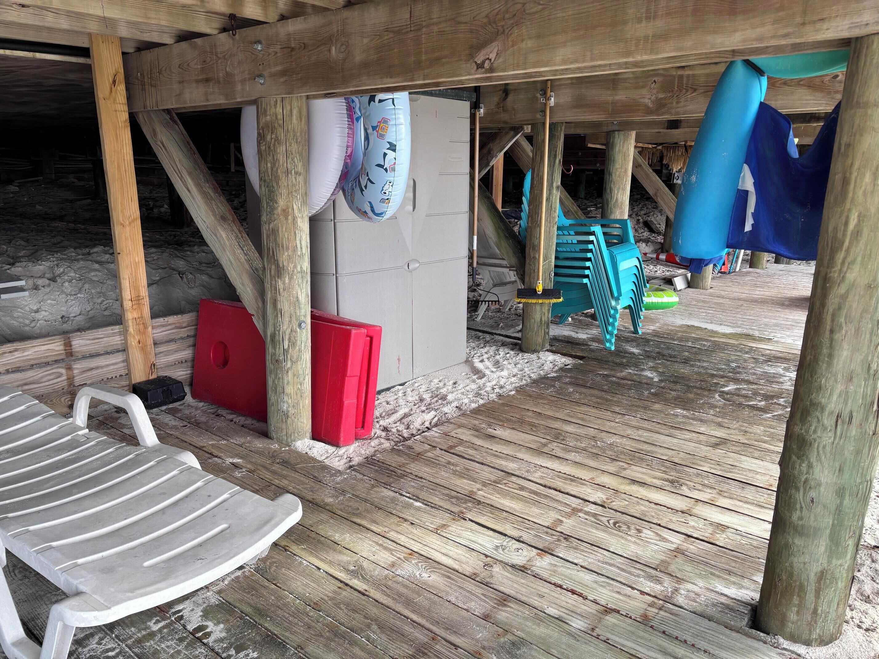 Eine Holzterrasse mit einem weißen Kunststoffstuhl, einer roten Aufbewahrungsbox und einer blauen Rutsche.