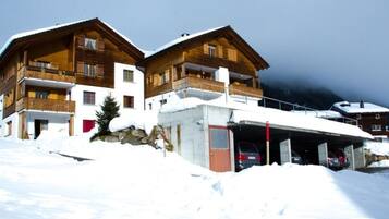 Ein zweistöckiges Holzhaus mit Balkonen, einem überdachten Parkplatz und einer verschneiten Landschaft.