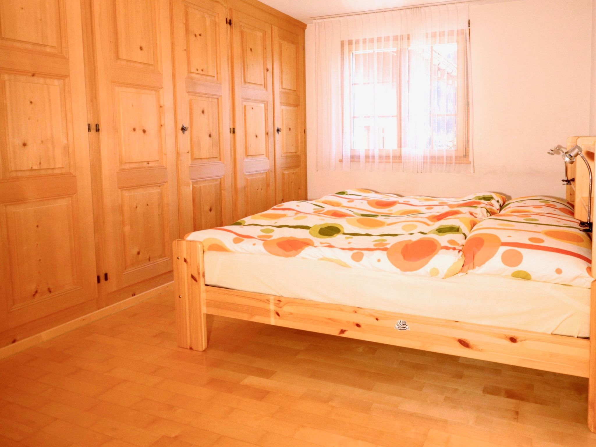 Une chambre à coucher avec un lit en bois, une armoire et une fenêtre avec des rideaux.