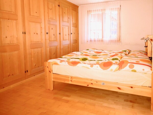 A bedroom with a wooden bed, a wardrobe, and a window with curtains.